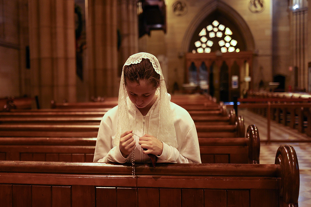 Young veiled woman praying the rosary inside a church