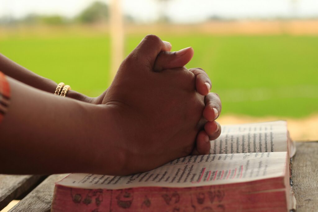 Catholic person praying with hands clasped on bible